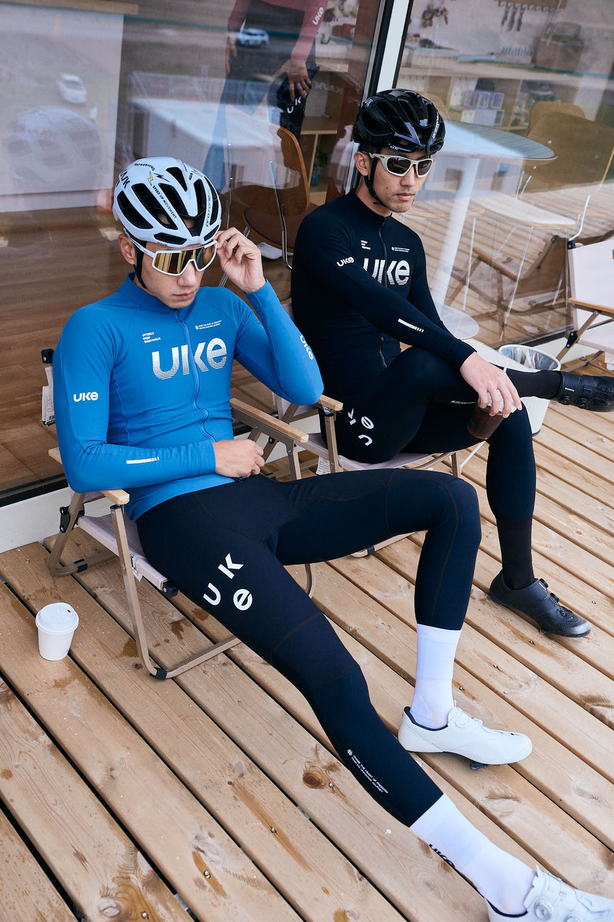 Deux cyclistes UKE portant des maillots à manches longues bleus et noirs et des cuissards à bretelles dans un café.