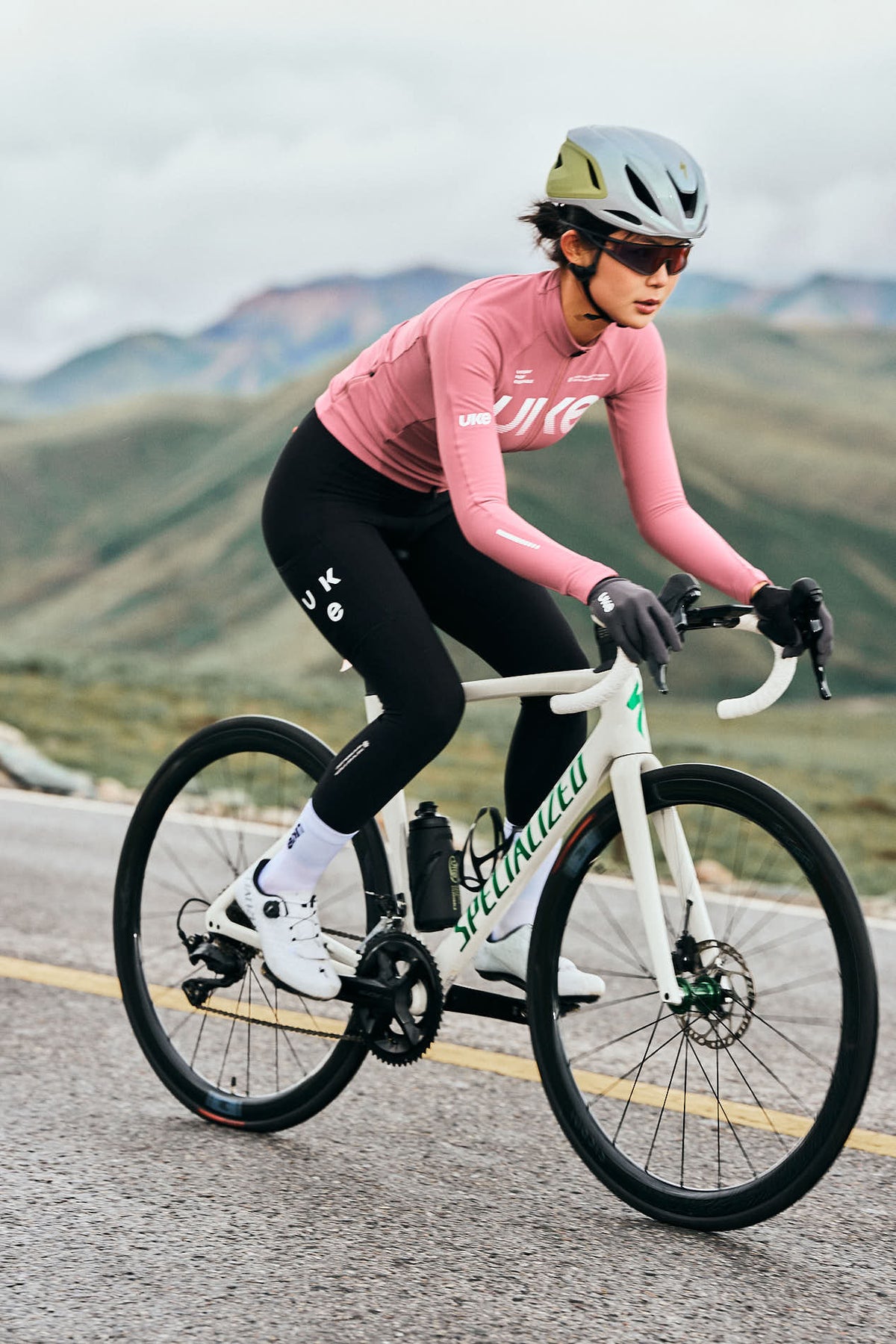 Un cycliste portant un maillot à manches longues UKE rose et un cuissard à bretelles noir sur la route.